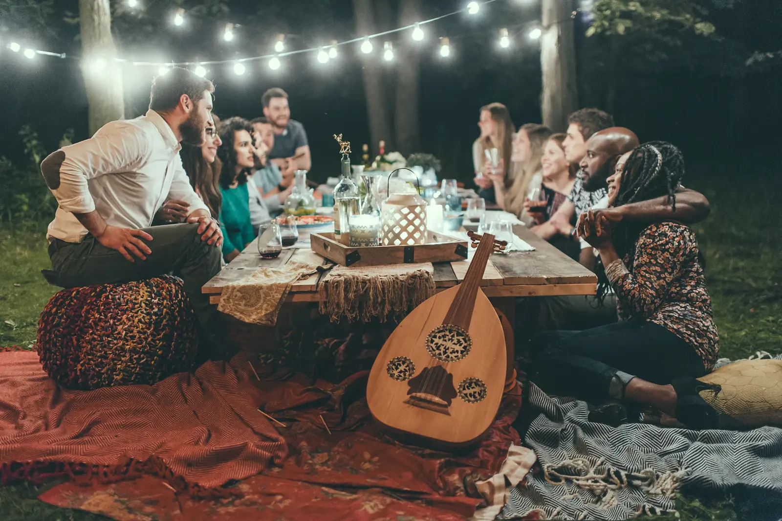 Friends at a long outdoor dinner table under string lights at night